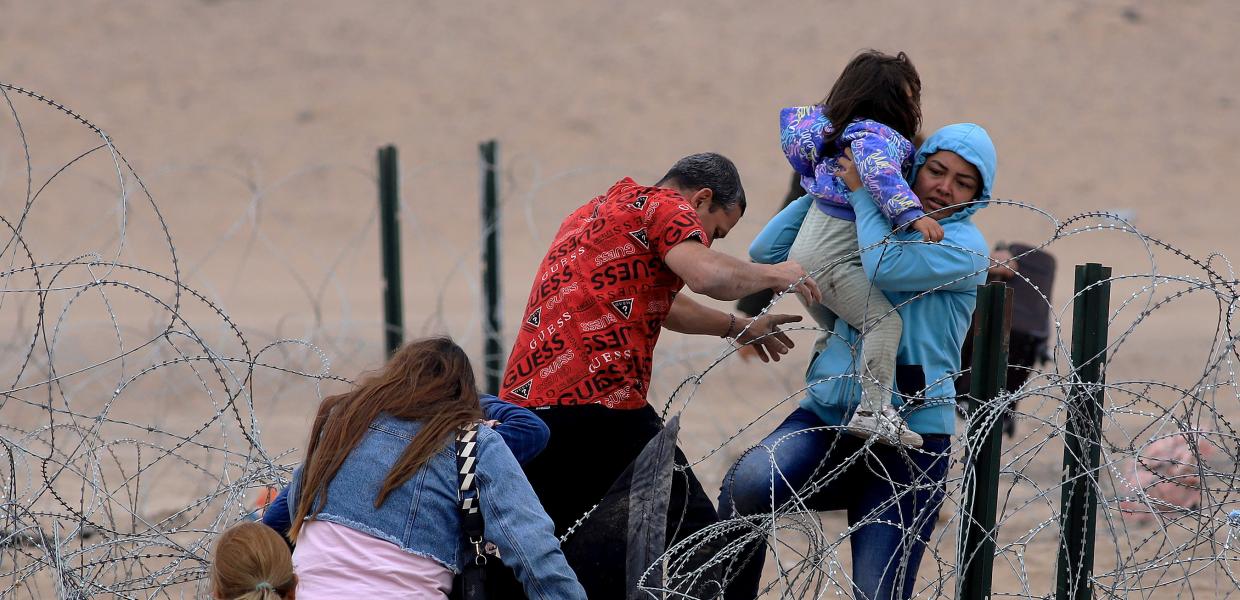 Μετανάστες με παιδάκι στα χέρια περνούν τα σύνορα στο Μεξικό μέσα από συρμάτινο πλέγμα