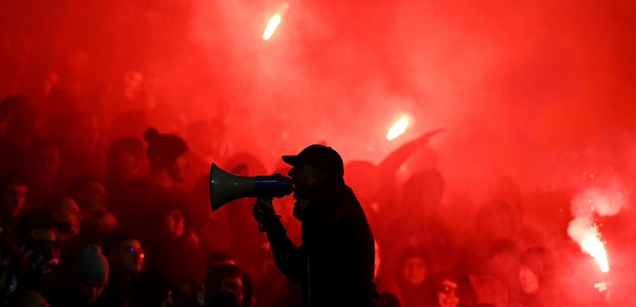 Οπαδοί σε εξέδρα σε κόκκινο φόντο από φωτοβολίδες