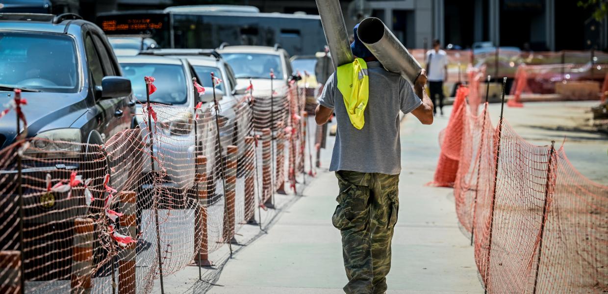 Εργάτης κουβαλάει μεταλλικό σωλήνα σε δρόμο 