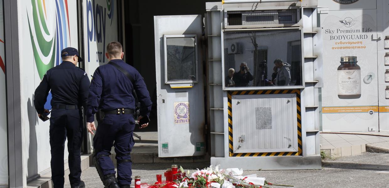 Αστυνομικοί περπατούν δίπλα στο φυλάκιο του ΑΤ Αγίων Αναργύρων με λουλούδια να είναι αφημένα μπροστά του για την 28χρονη Κυριακή που δολοφονήθηκε στο σημείο