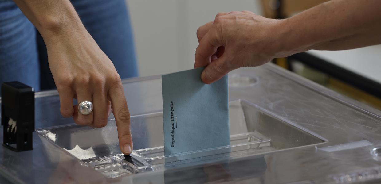 Χέρι ψηφοφόρου σπρώχνει φάκελο στην κάλπη - Γαλλικές Εκλογές 2024