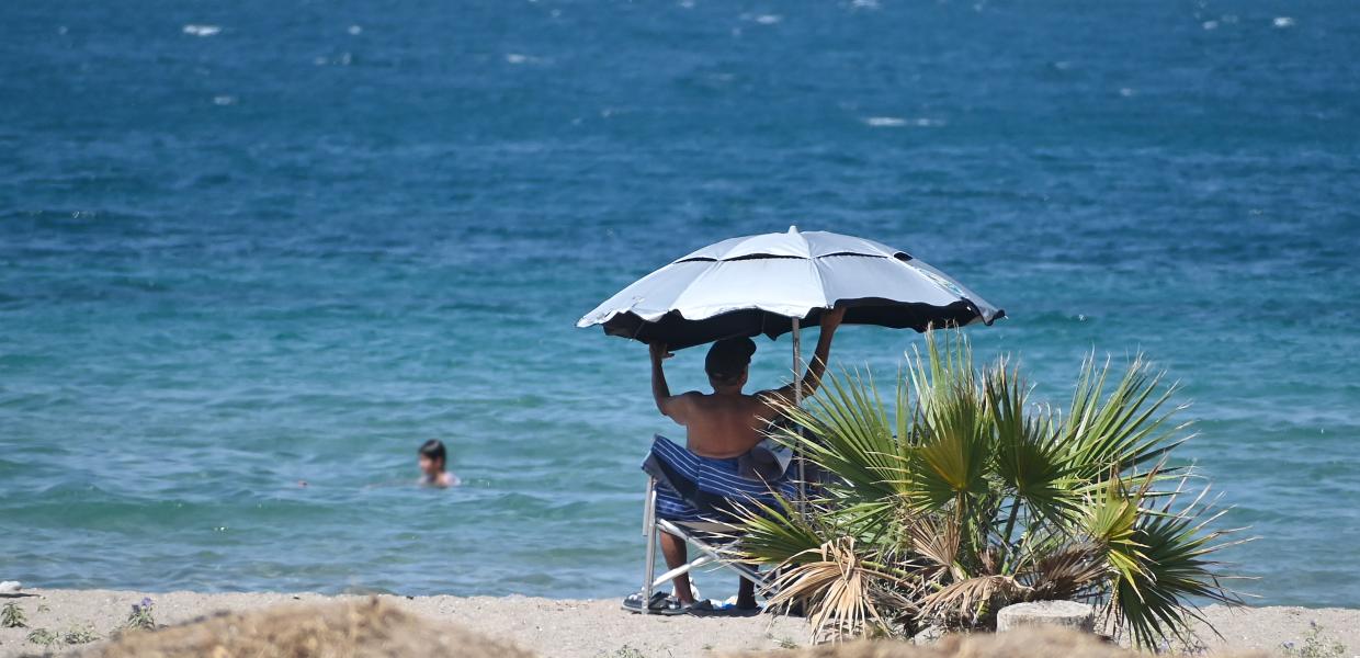 άντρας κάθεται κάτω από ομπρέλα στη θάλασσα