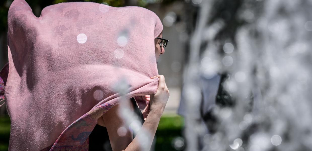 Γυναίκα σκεπασμένη με μαντήλι στο κεφάλι περνά μπροστά από συντριβάνι