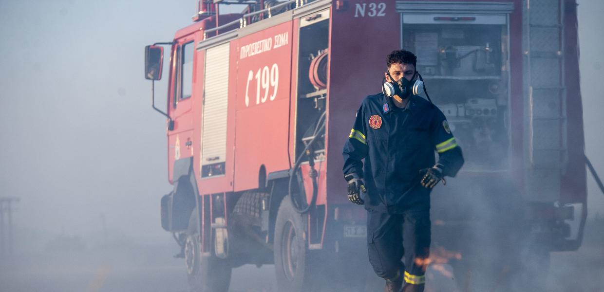 Πυροσβέστης μπροστά από πυροσβεστικό όχημα κατά την κατάσβεση φωτιάς