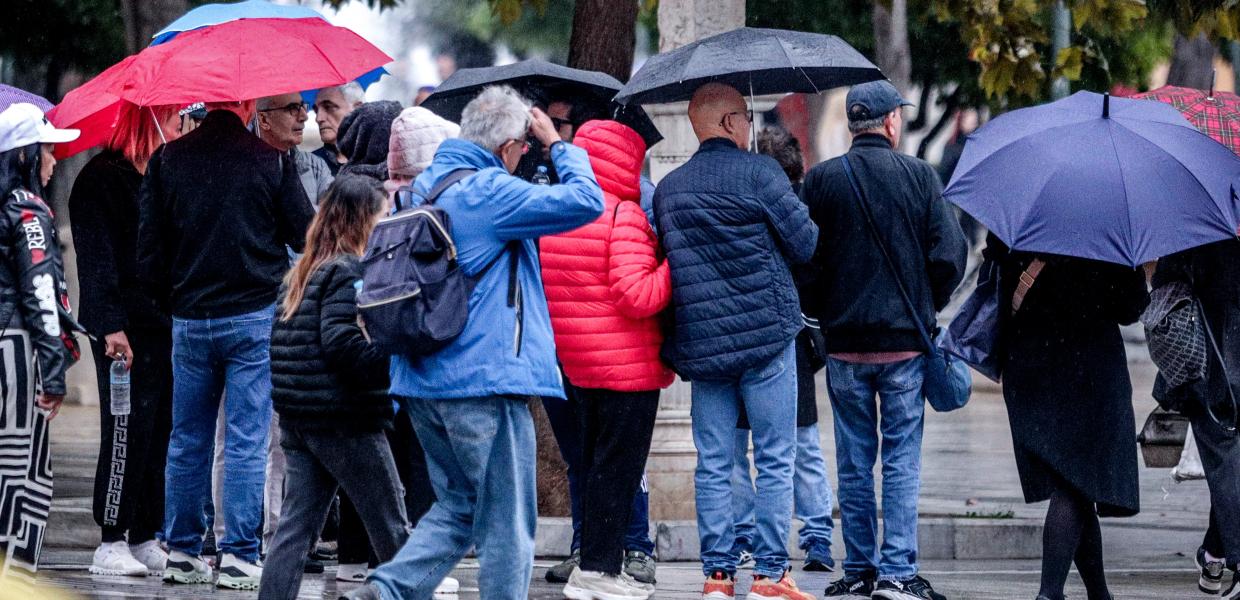 Κόσμος με μπουφάν και ομπρέλες στον δρόμο