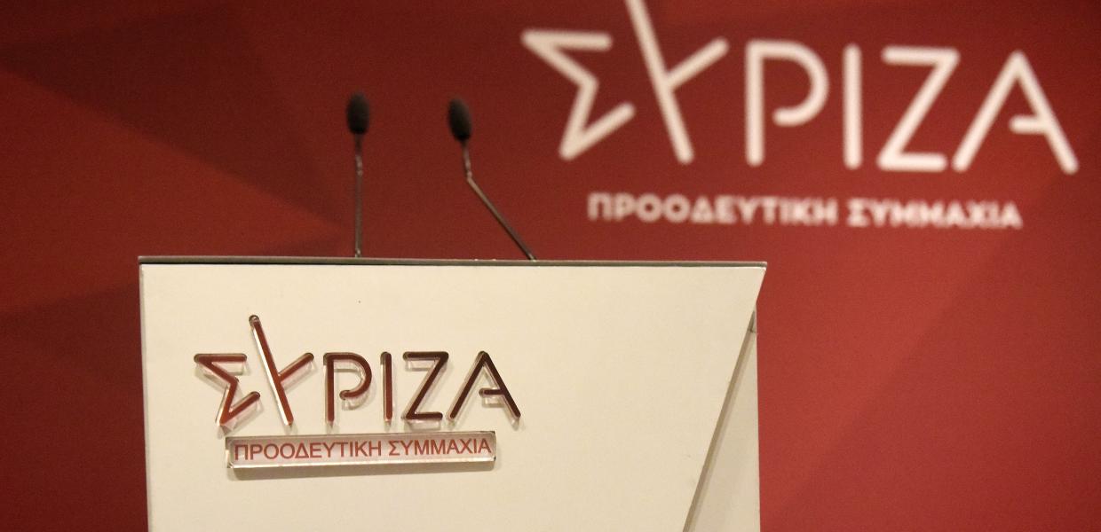 Πόντιουμ με μικρόφωνα και το σήμα του ΣΥΡΙΖΑ-ΠΣ