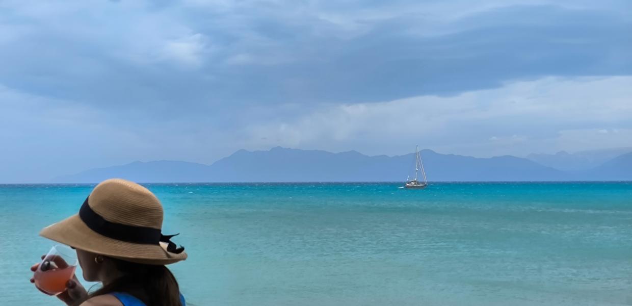 Γυναίκα απολαμβάνει ρόφημα μπροστά από συννεφιασμένη παραλία