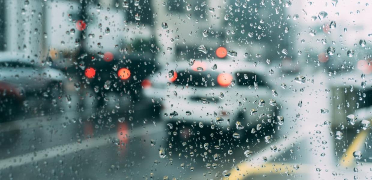 Σταγόνες βροχής σε τζάμι και στο βάθος αυτοκίνητα σε δρόμο με κίνηση