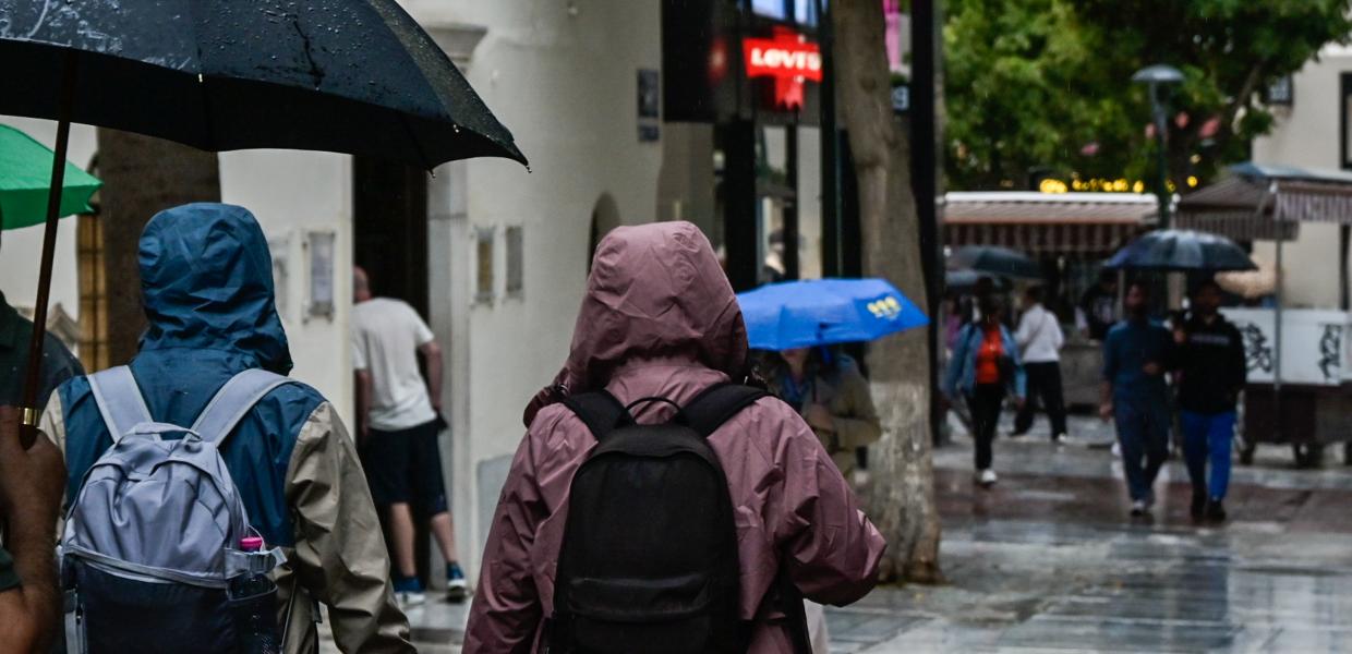 Κόσμος περπατά στην Ερμού με βροχή