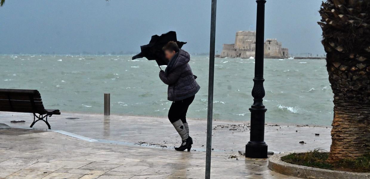 Γυναίκα δίπλα στη θάλασσα με ομπρέλα που την παίρνει ο αέρας