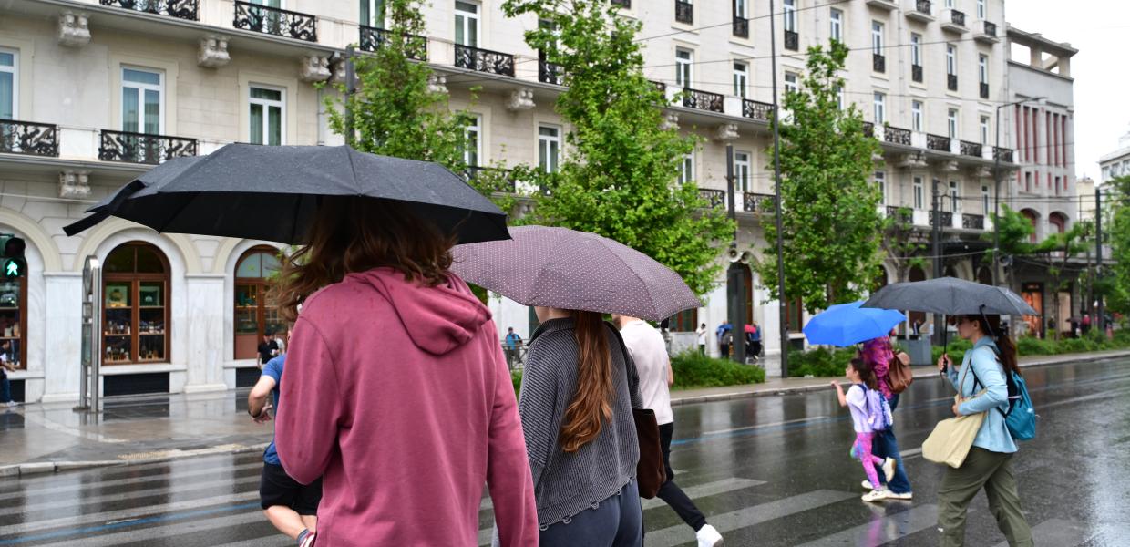 Κόσμος περπατά με ομπρέλες σε δρόμο της Αθήνας