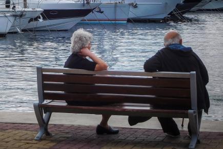 Ζευγάρι ηλικιωμένων κάθεται γυρισμένο πλάτη σε ένα παγκάκι με θέα την θάλασσα